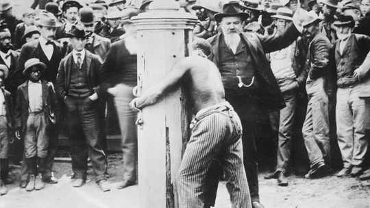 На фотографии шериф, осуществляет порку негра, прикованного к..0