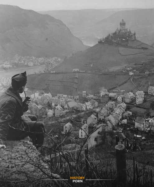 Американский солдат курит на выступе с видом на немецкий город..0